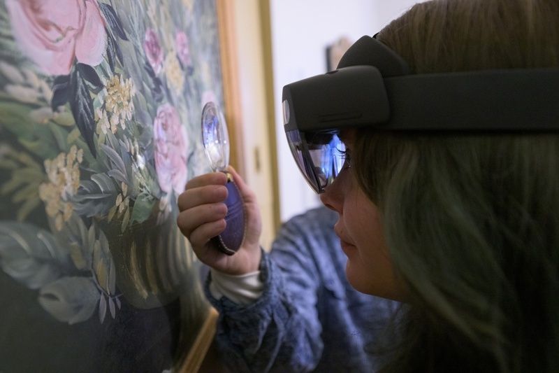 Person untersucht ein Blumenbild mit Lupe und Datenbrille